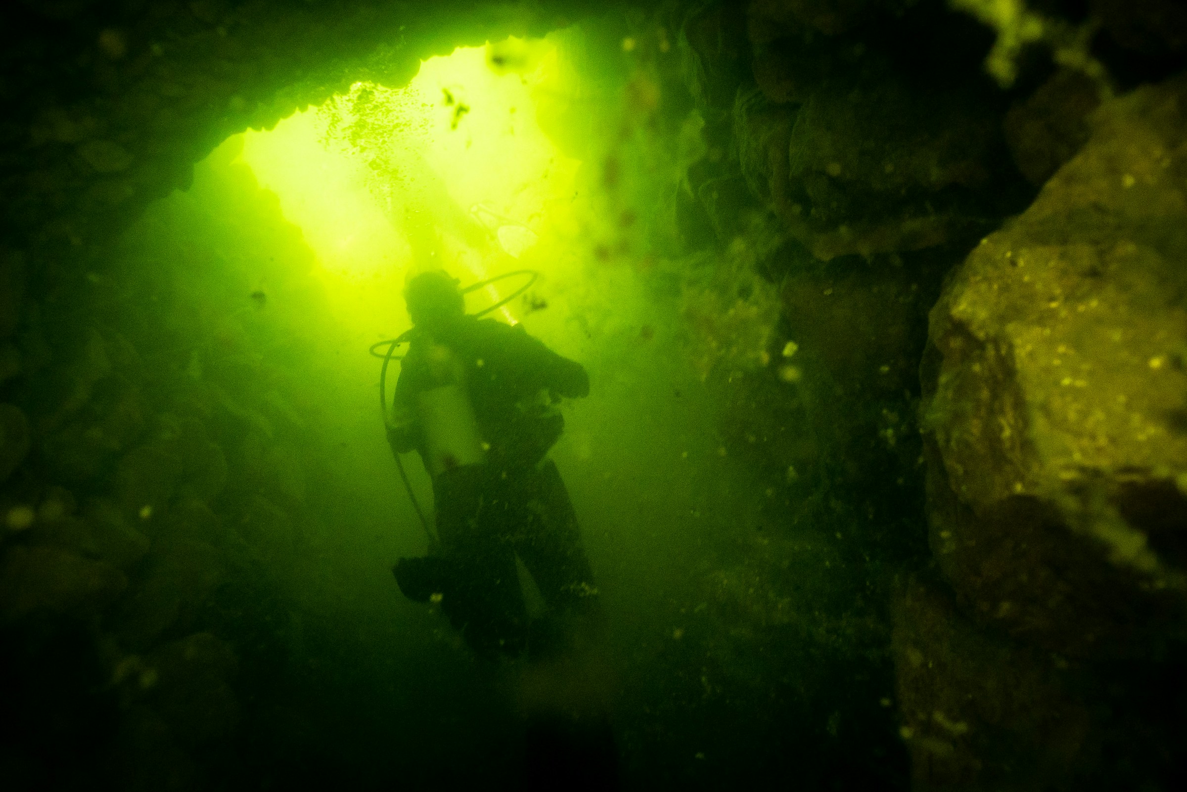Scuba diver navigating a dark underwater cave lit by a single green light