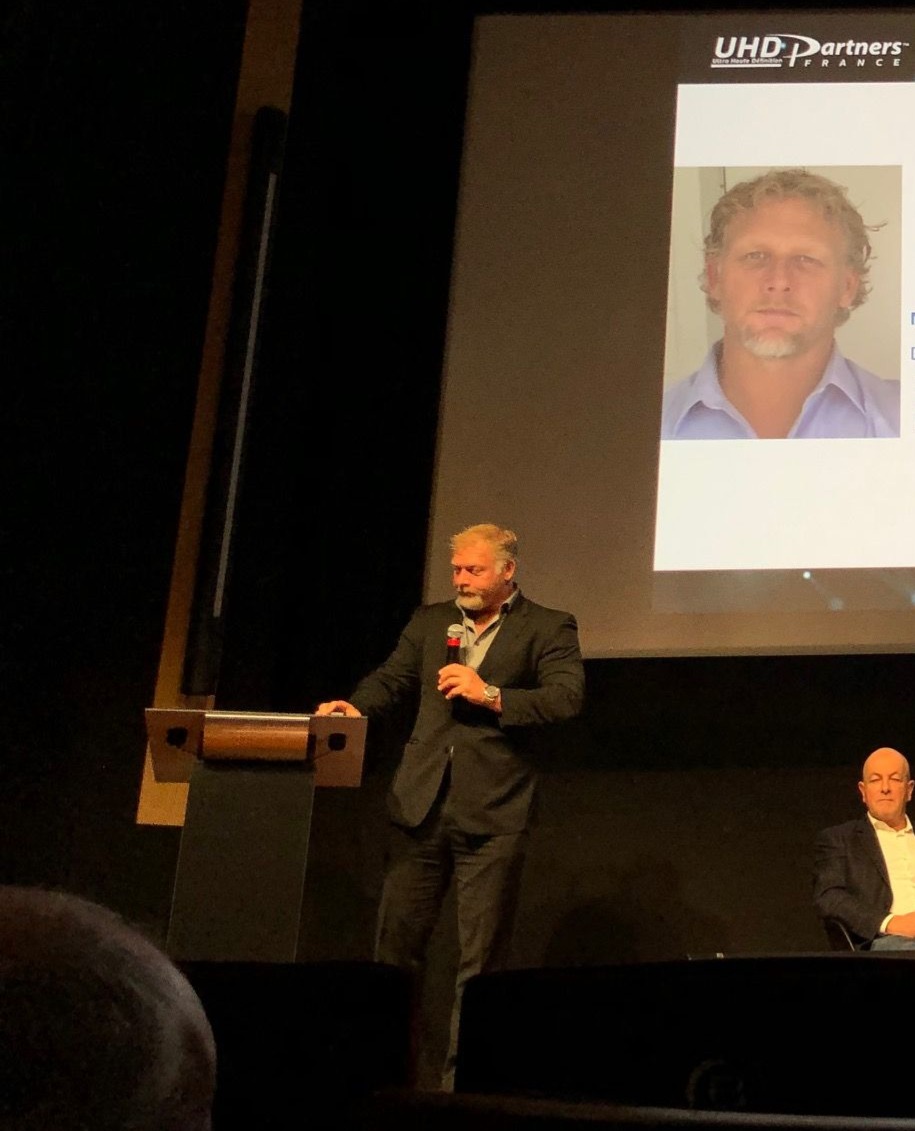 Michael Hoog presenting at podium with his headshot projected on screen behind him